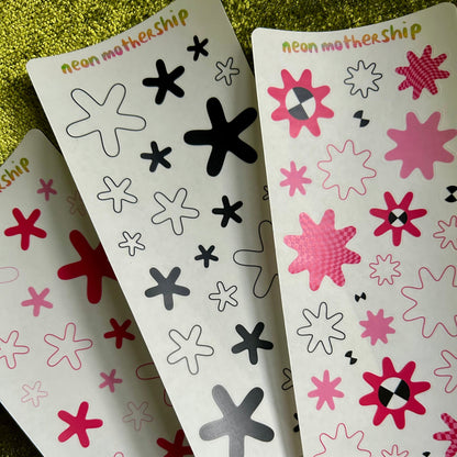 Three sheets of decorative stickers with star and flower patterns on a green textured surface.