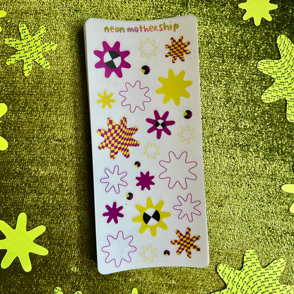 Sheet of colorful star-shaped stickers on a green textured background with additional star stickers.
