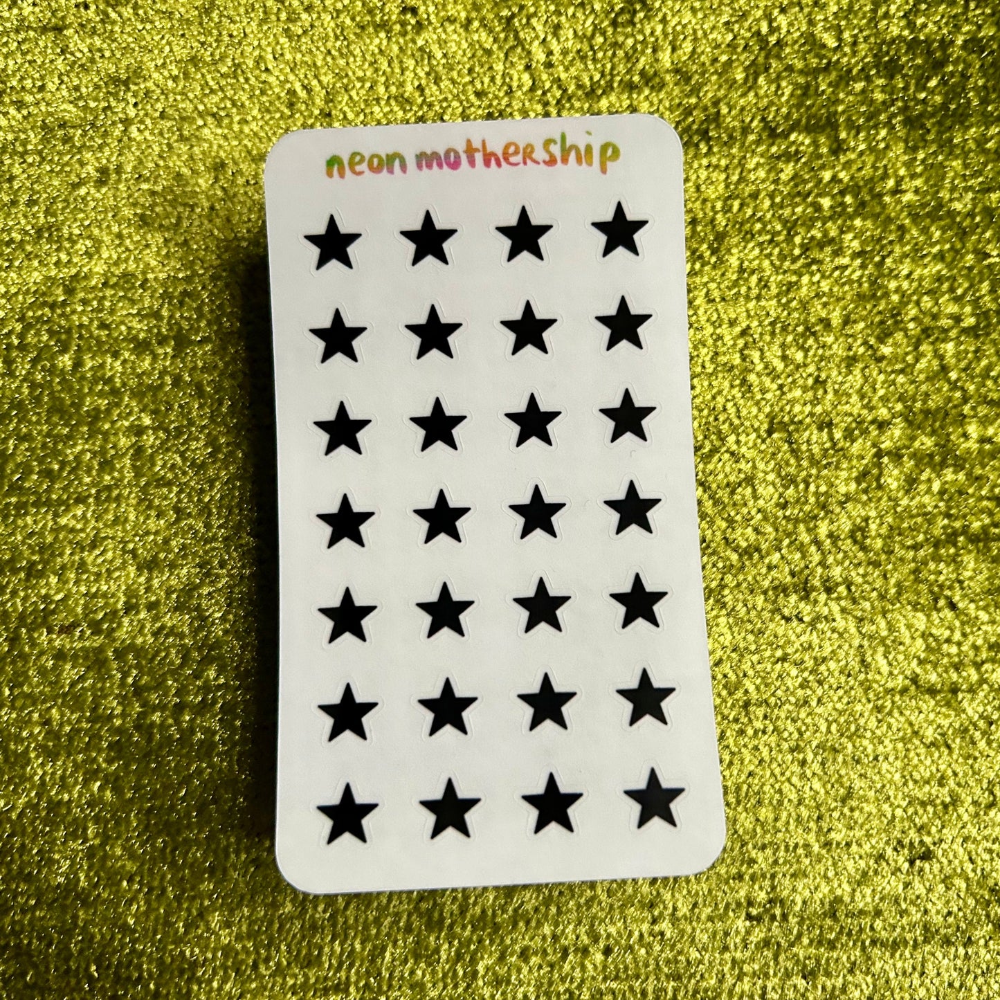 Sheet of black star-shaped stickers on a green textured background