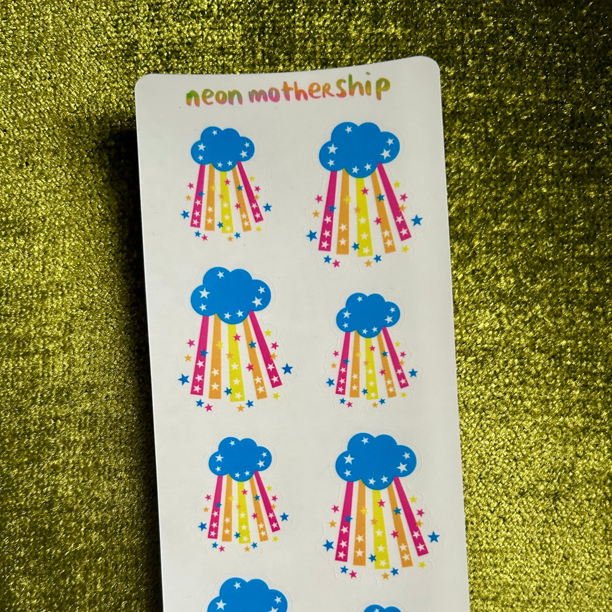 Sheet of colorful cloud and rainbow stickers on a green textured surface