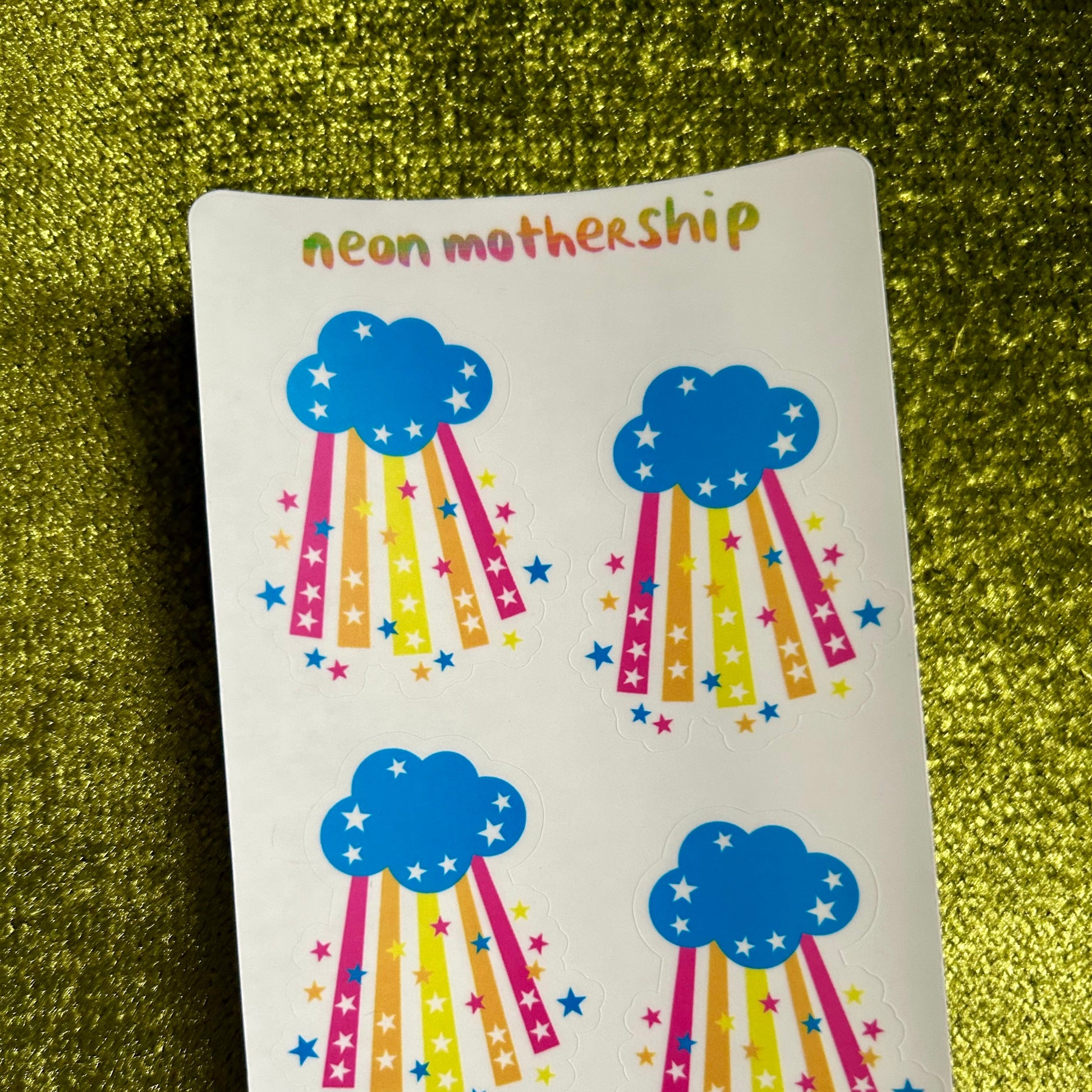 sticker sheet with blue cloud designs and colorful rainbows on a green textured background