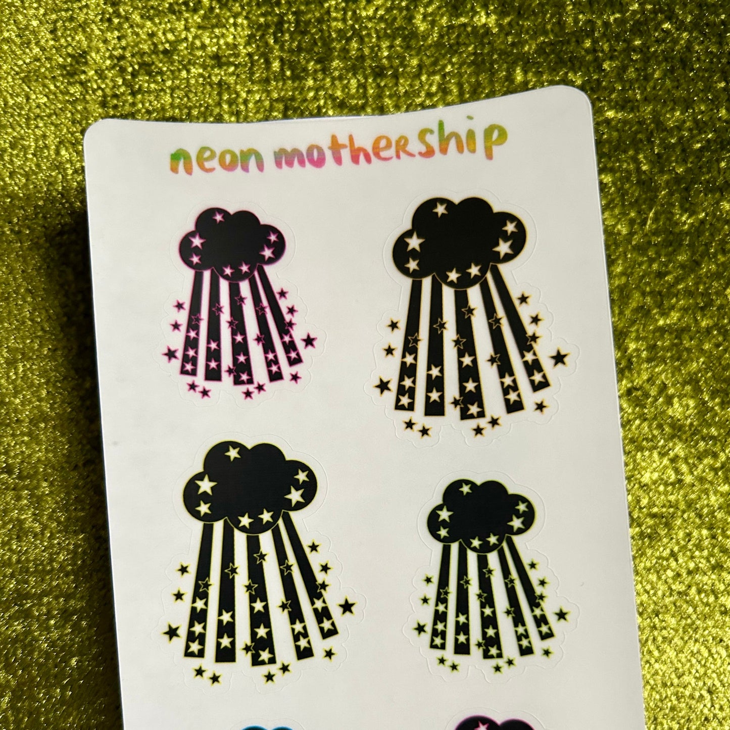 Sheet of cloud-shaped stickers with star details on a green glittery background, branded 'neon mothership'.