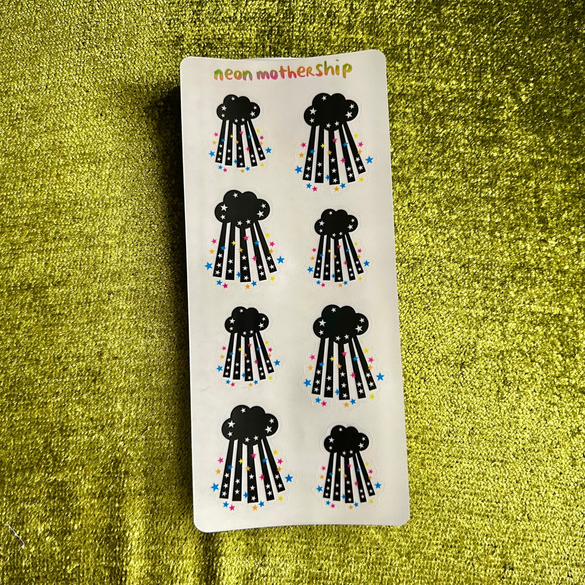 Sheet of black cloud-shaped stickers with colorful details on a green textured background