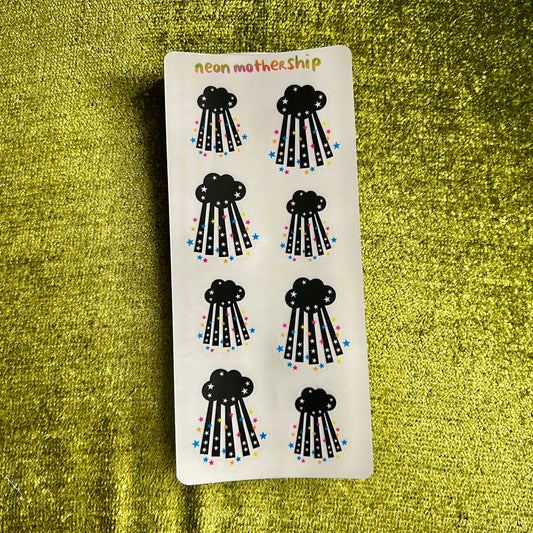 Sheet of black cloud-shaped stickers with colorful details on a green textured background