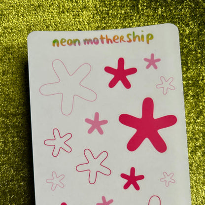 sticker sheet with red and pink star-shaped stickers on a green glittery background