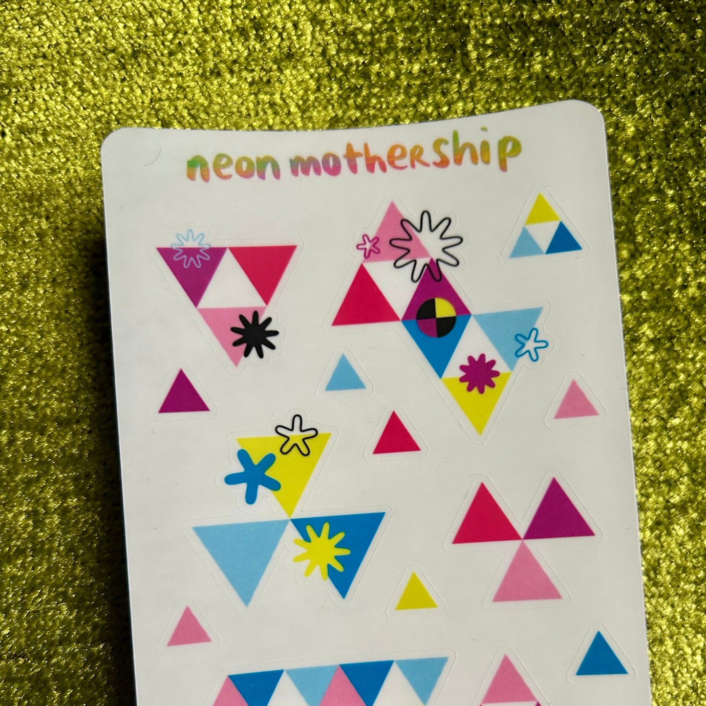 Colorful geometric patterned sticker sheet with 'neon mothership' text on a green textured background