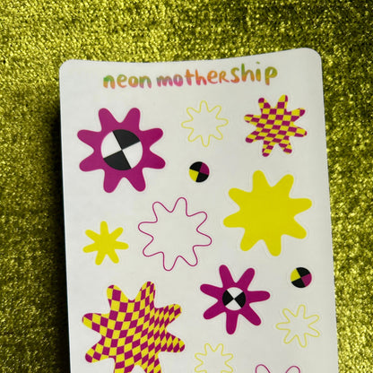 Sheet of colorful star-shaped stickers with 'neon mothership' branding on a green glittery background.