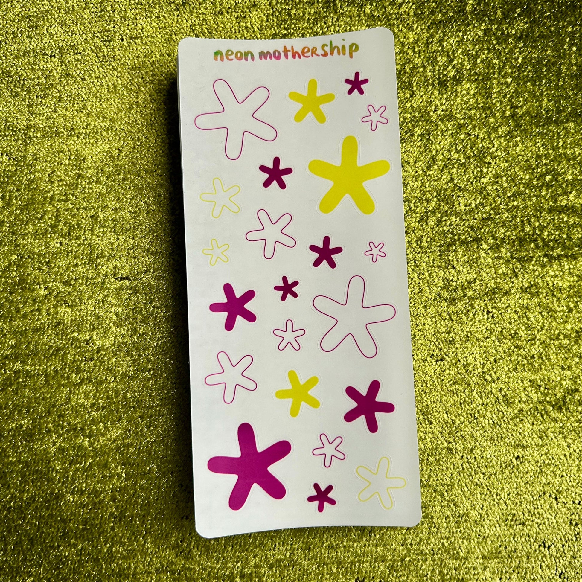 Sheet of star-shaped stickers with pink, yellow, and purple colors on a green textured background.