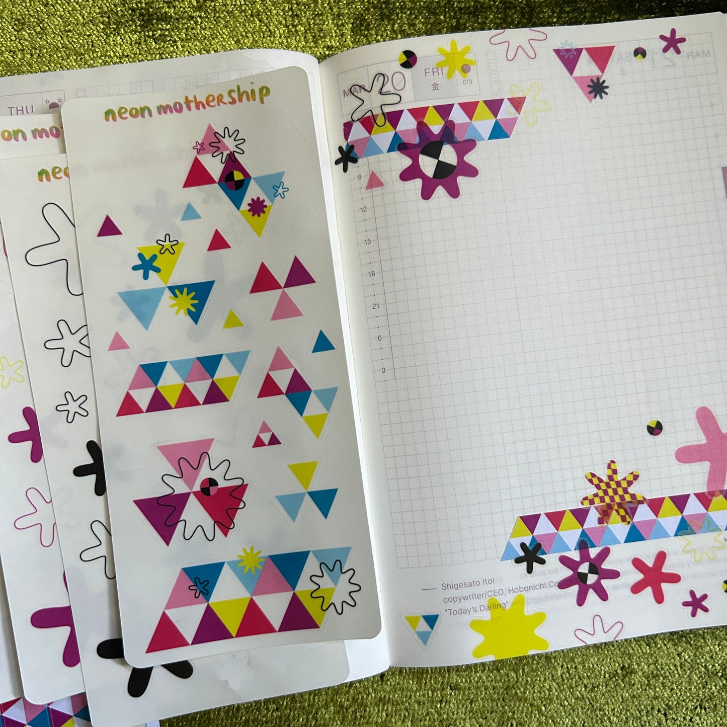 Colorful geometric stickers in a notebook page lying on a green textured surface