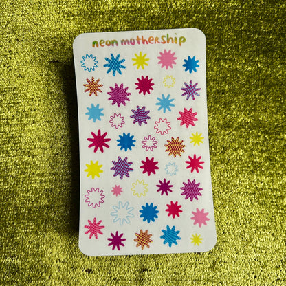 Sticker sheet with colorful starburst designs on a green textured surface