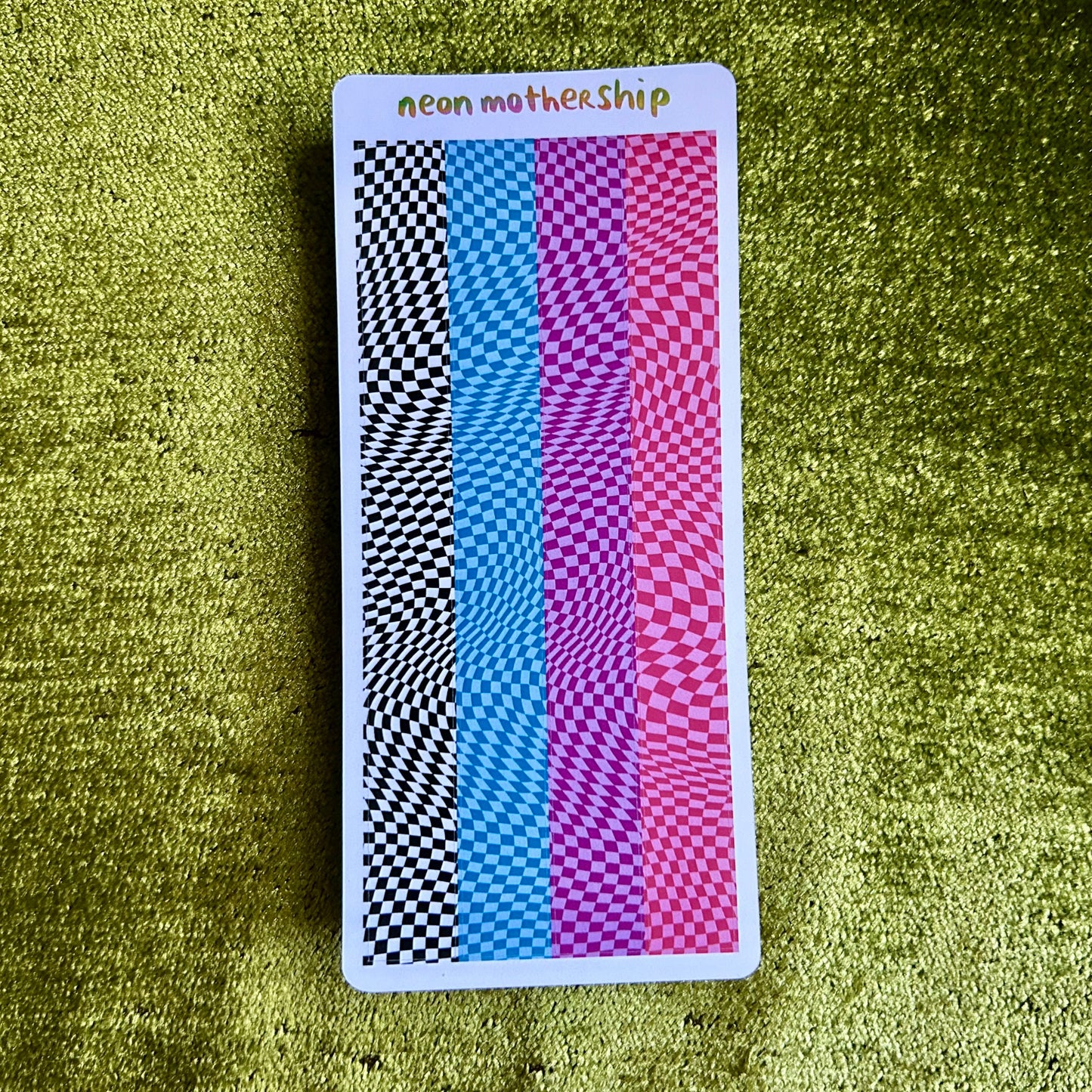 Colorful checkered sticker sheet with 'neon mothership' text on a green textured surface