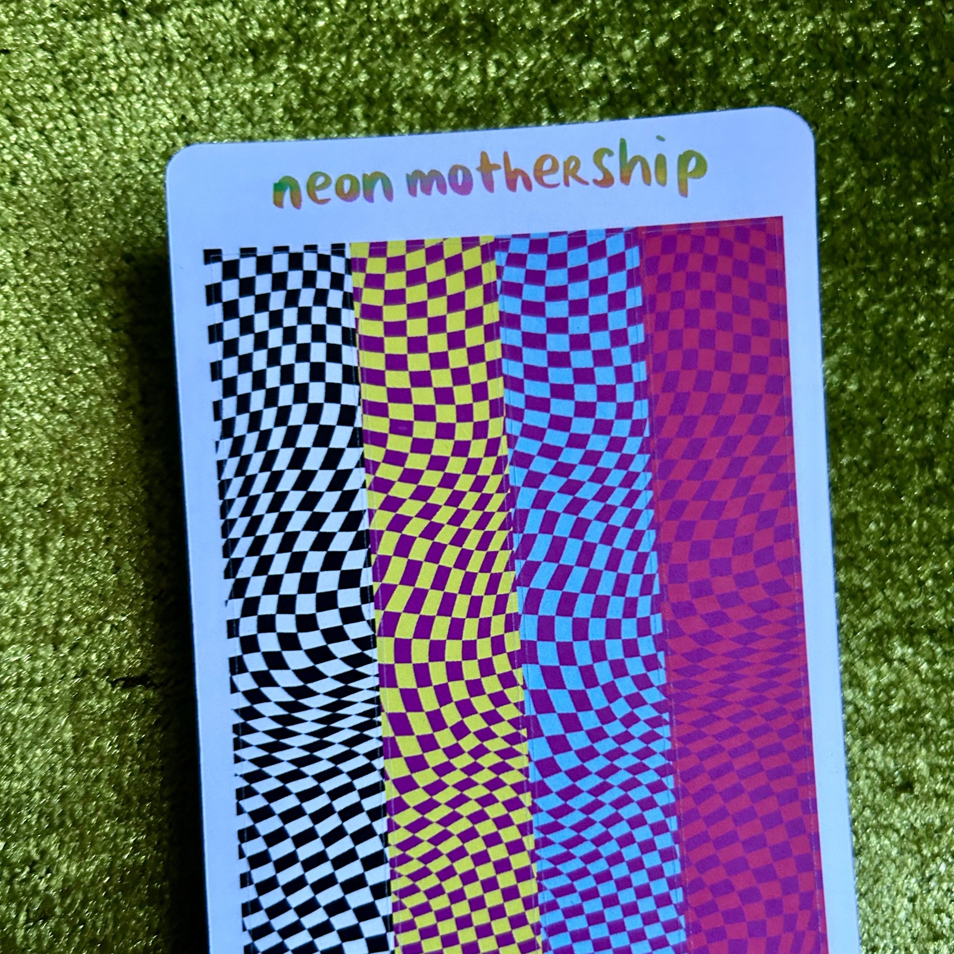 sticker sheet with checkered patterns and 'neon mothership' text on a green textured surface
