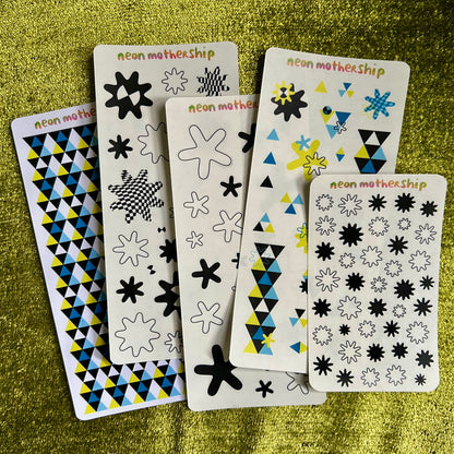 Set of five patterned sticker sheets on a green textured surface