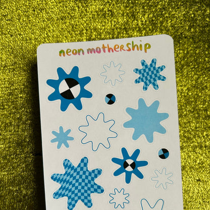 Sheet of blue star-shaped stickers with 'neon mother ship' branding on a green glittery background.