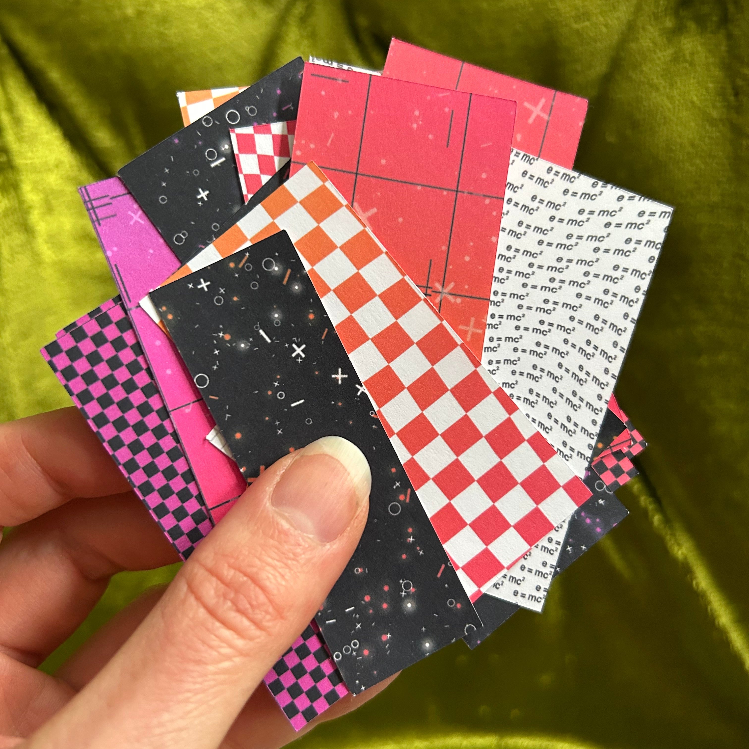 Hand holding a stack of colorful patterned paper squares against a green fabric background