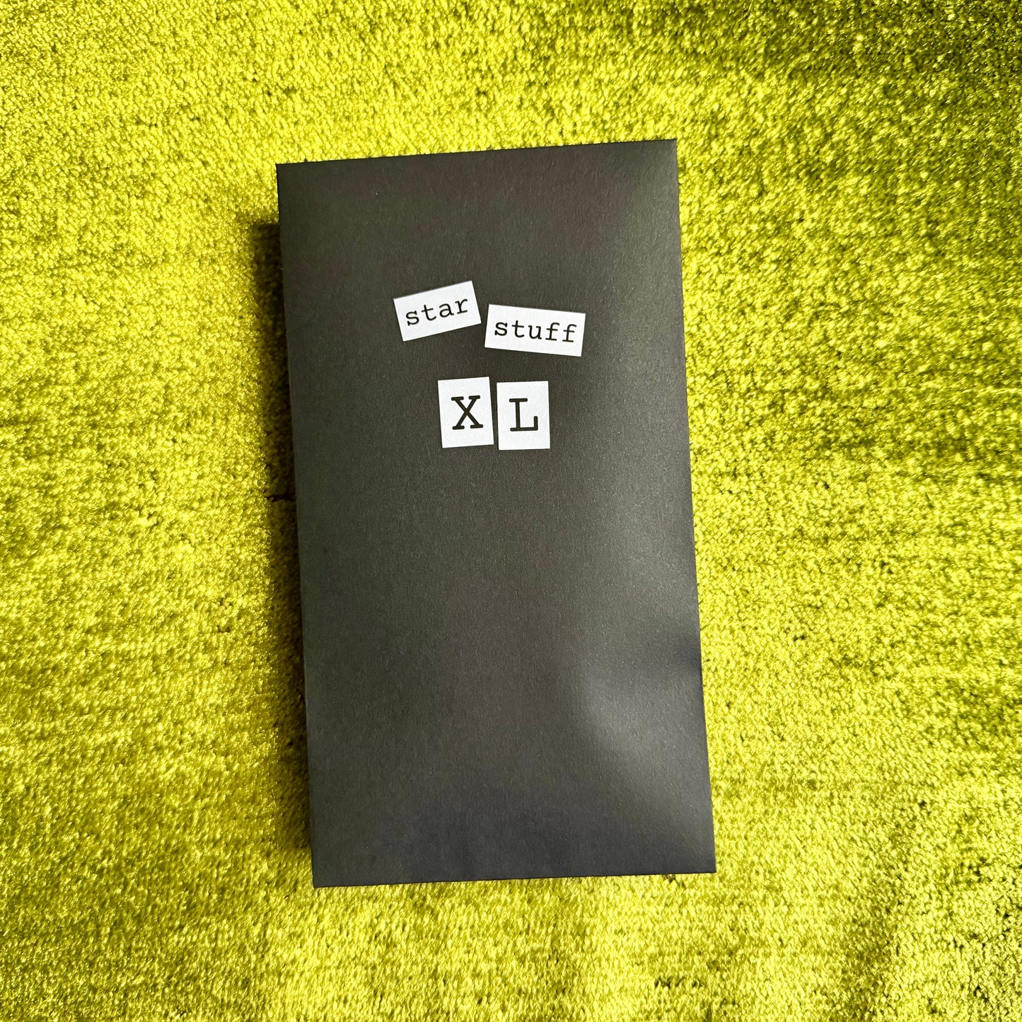 Black rectangular envelope with 'star stuff XL' text on a green textured surface