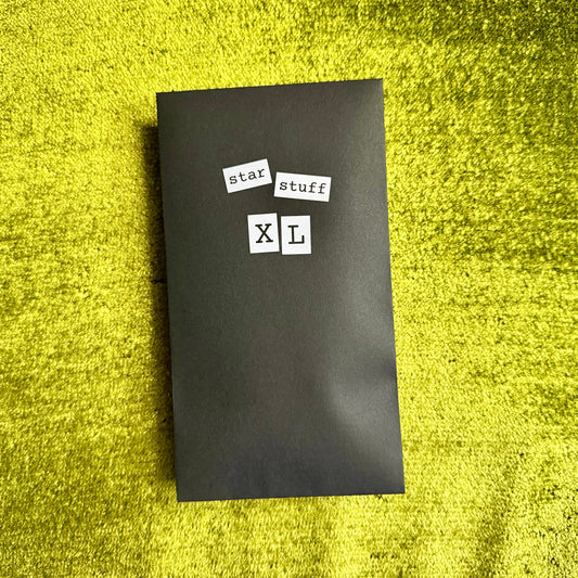 Black rectangular envelope with 'star stuff XL' text on a green textured surface