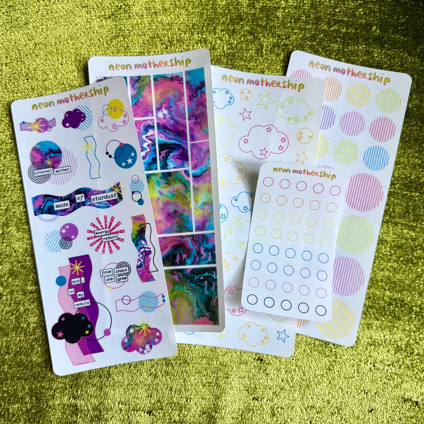 Colorful sticker sheets from 'neon motherShips' on a green textured surface