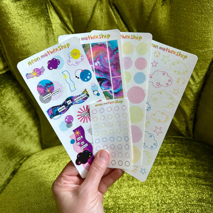 Hand holding a set of colorful sticker sheets against a green textured background