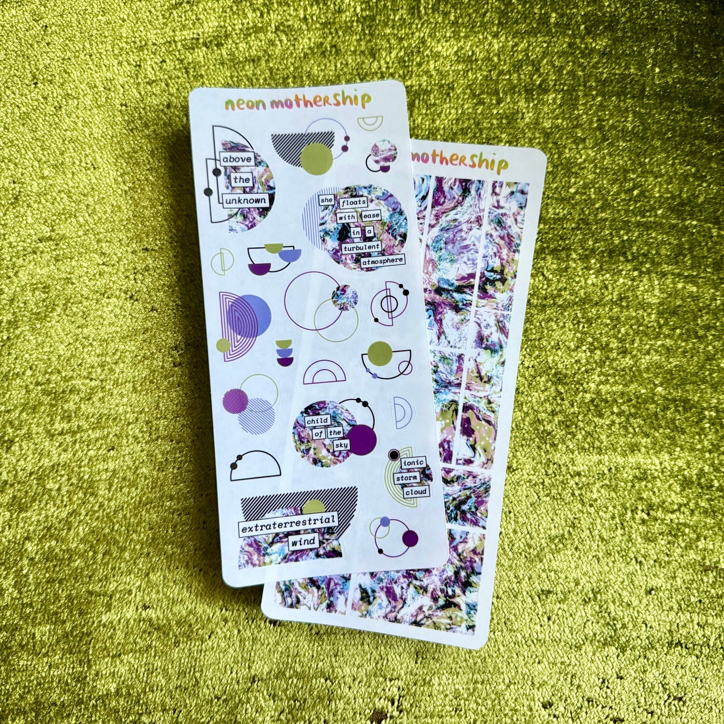 Two sheets of colorful stickers on a green textured surface