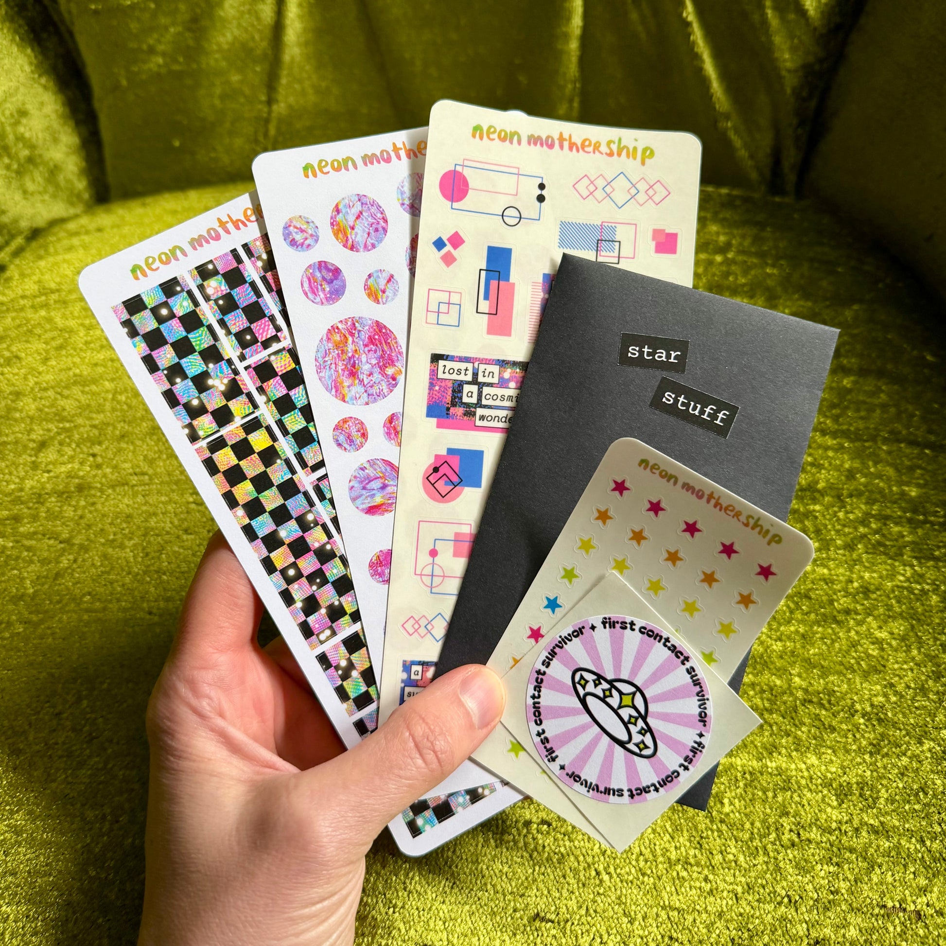 Hand holding a collection of colorful sticker sheets against a green fabric background