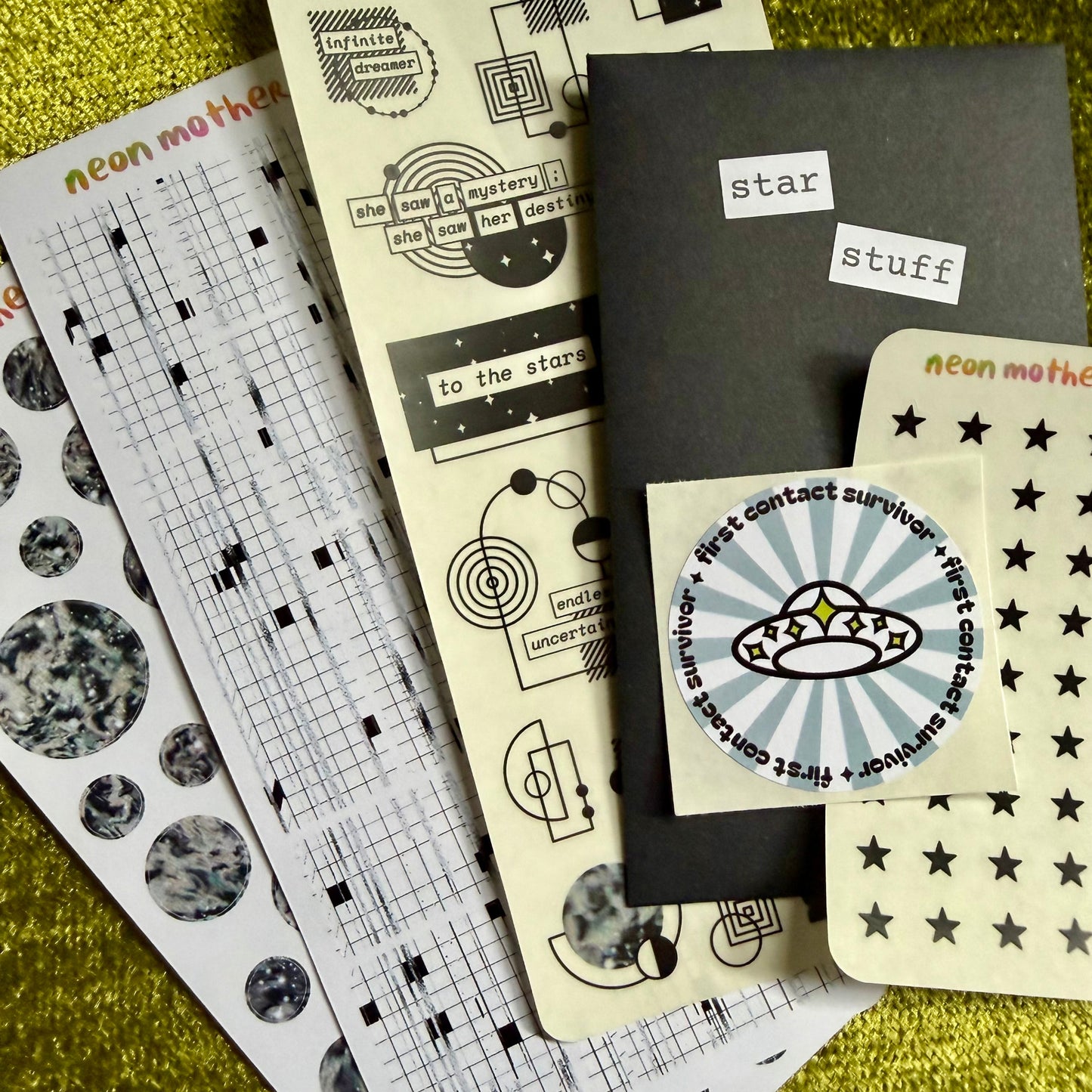 Collection of stationery items including sticker sheets on a textured green surface