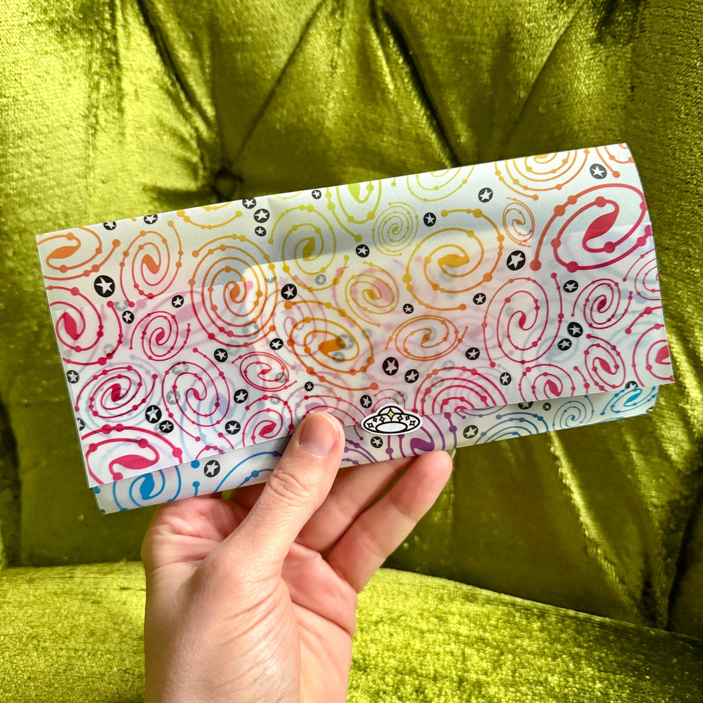 Hand holding a colorful patterned vellum envelope against a green fabric background