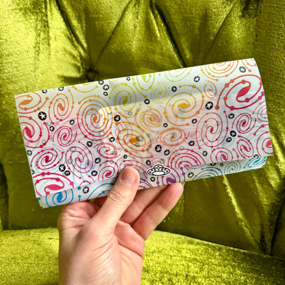 Hand holding a colorful patterned vellum envelope against a green fabric background