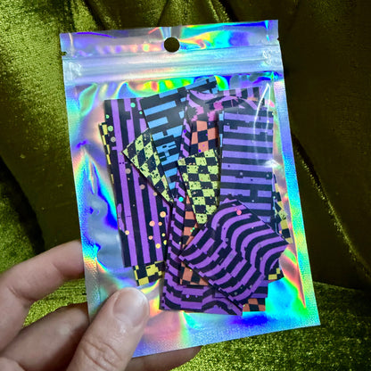 hand holding small holographic bag with foiled sticker scraps on a green background