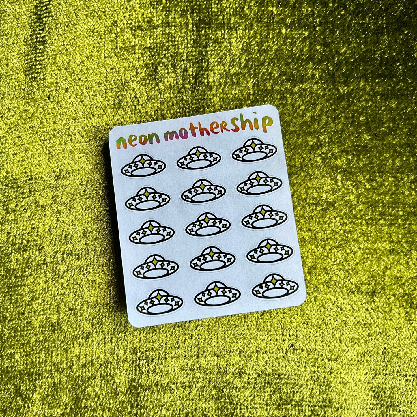 Sheet of stickers with black illustrations on a white card, labeled 'neon mothership', against a green textured background.