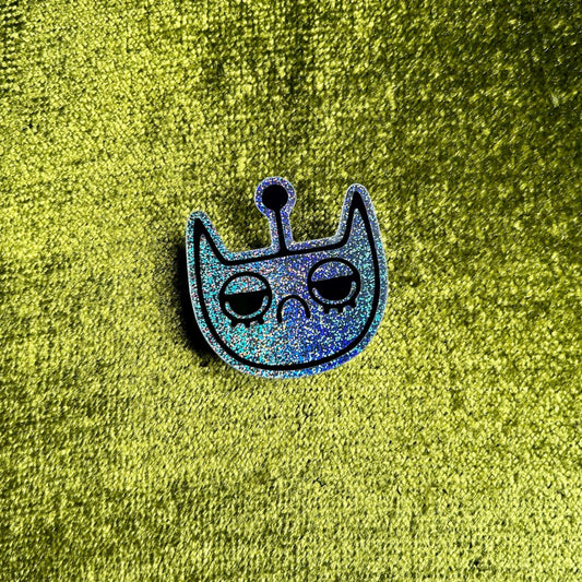 Silver holographic spacecat sticker on a green textured background