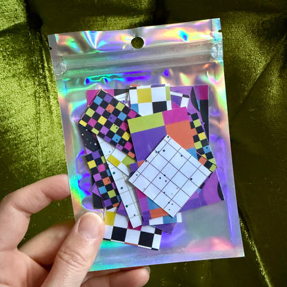 hand holding a small holographic package of colorful sticker scraps against a green background