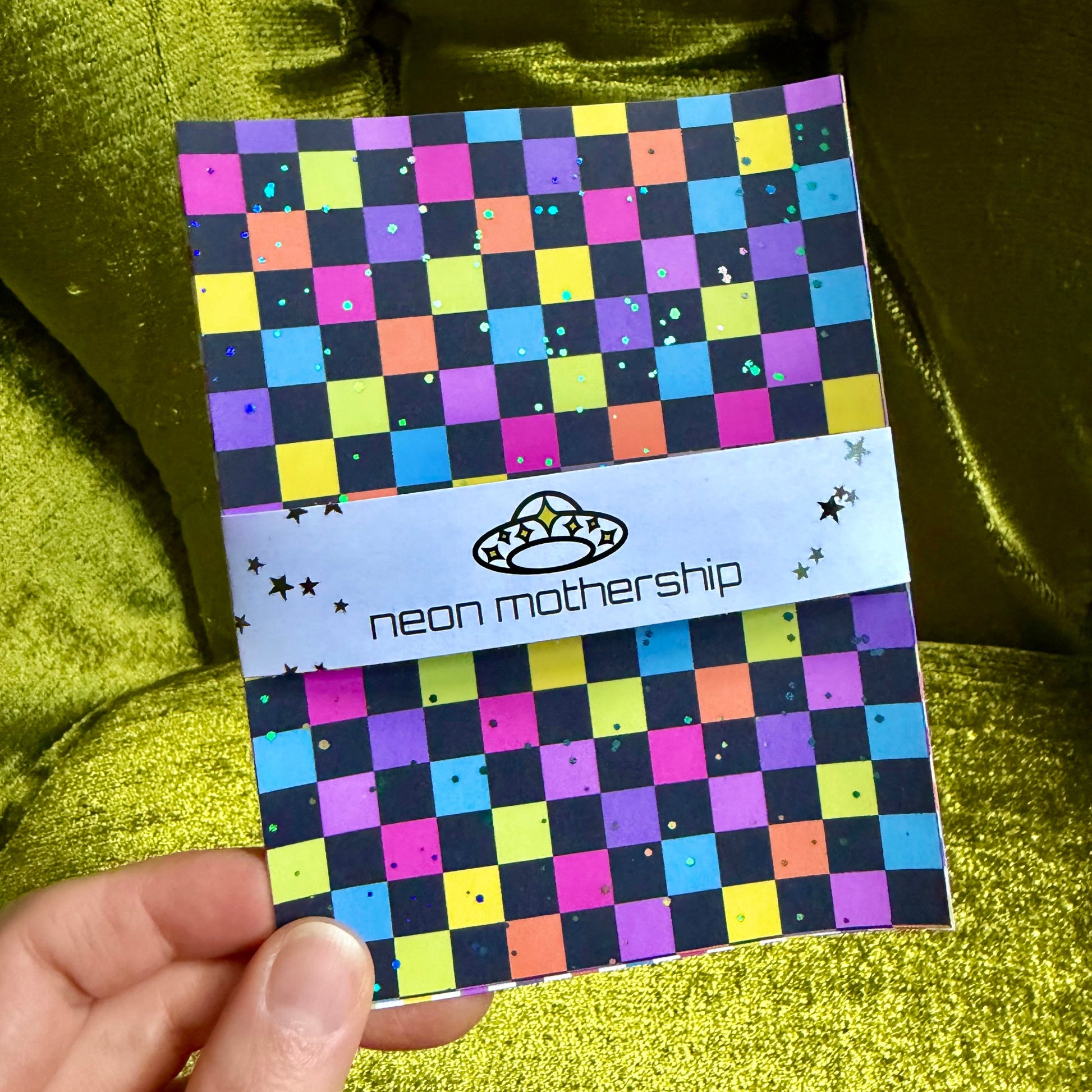 hand holding a glittering checkered sticker sheet on a green background