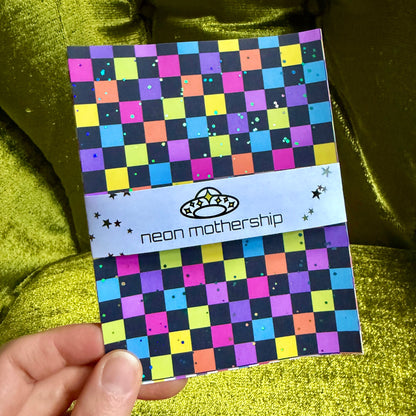 hand holding a glittering checkered sticker sheet on a green background
