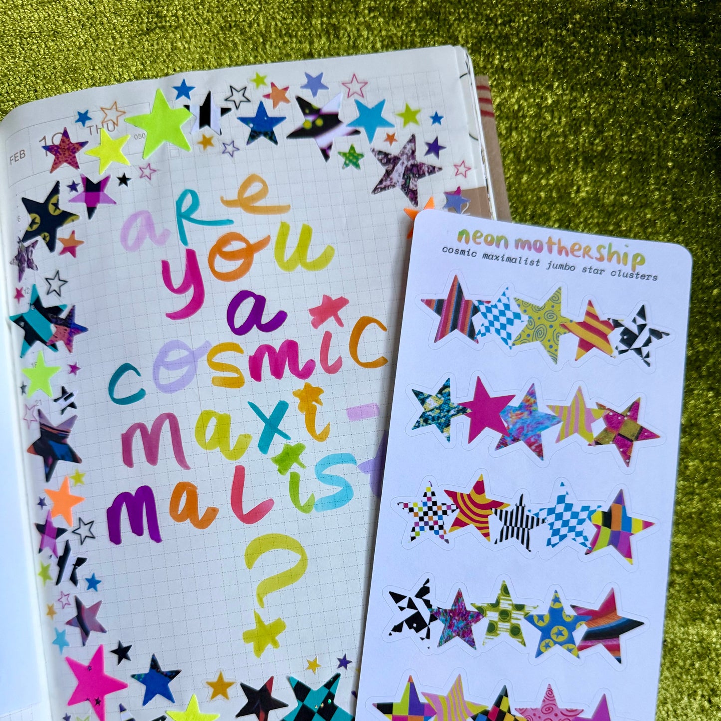 Colorful star-themed notebook and sticker sheet on a green textured surface