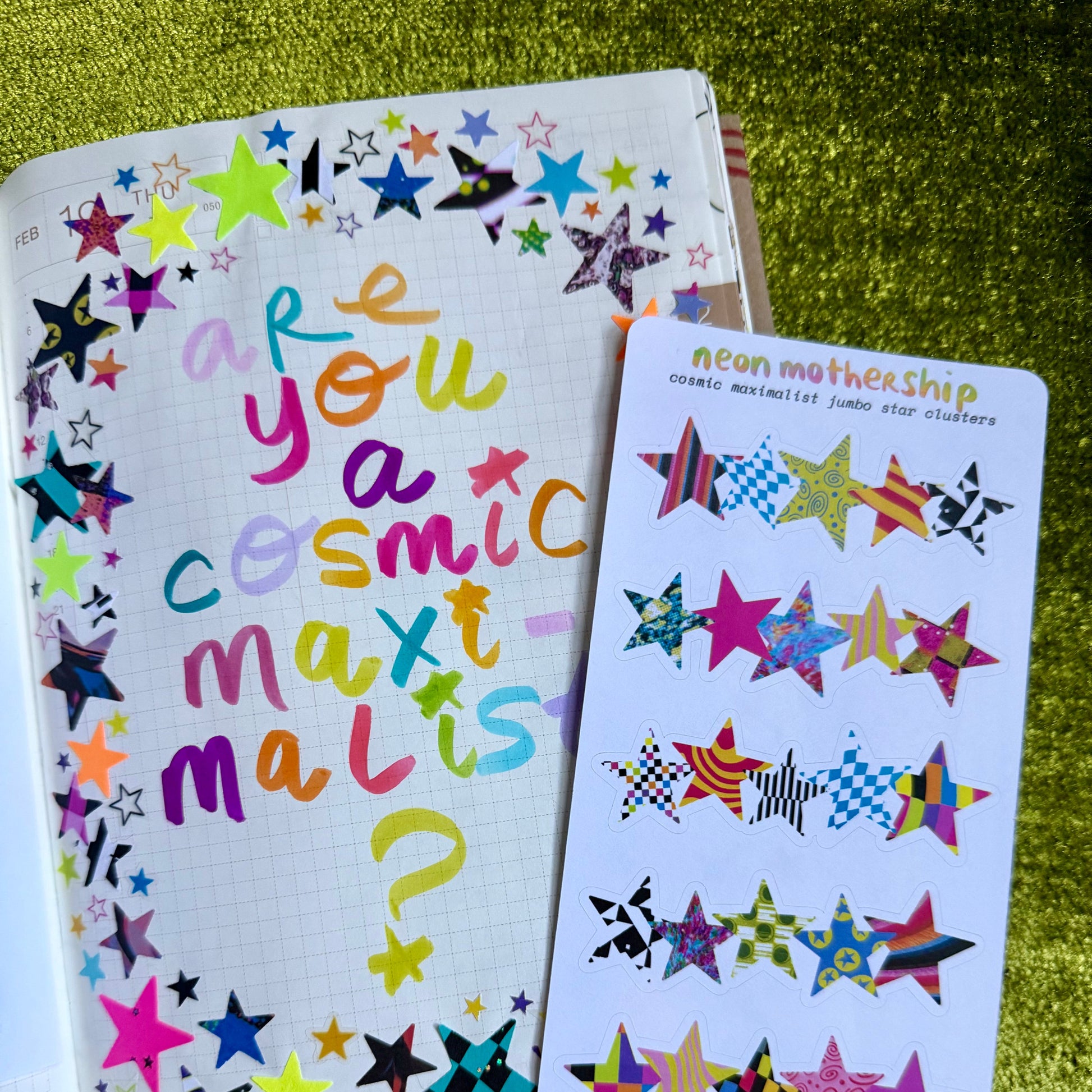 Colorful star-themed notebook and sticker sheet on a green textured surface