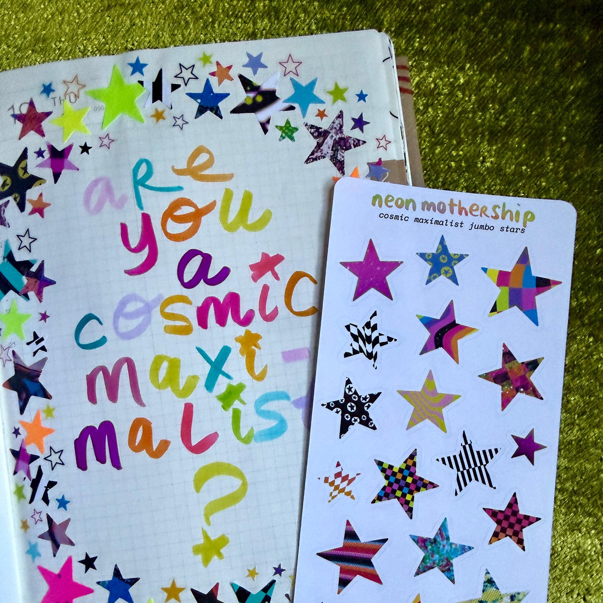 Colorful star-themed notebook and sticker sheet on a green textured surface