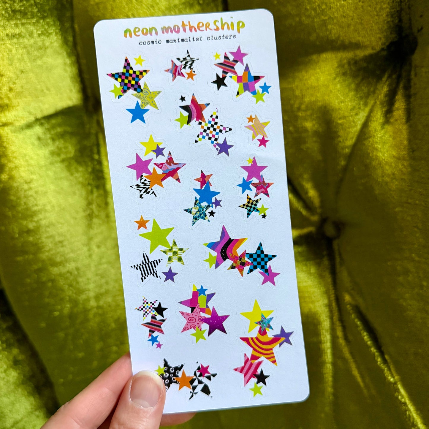 sticker sheet with colorful star-shaped stickers held by a hand against a green fabric background
