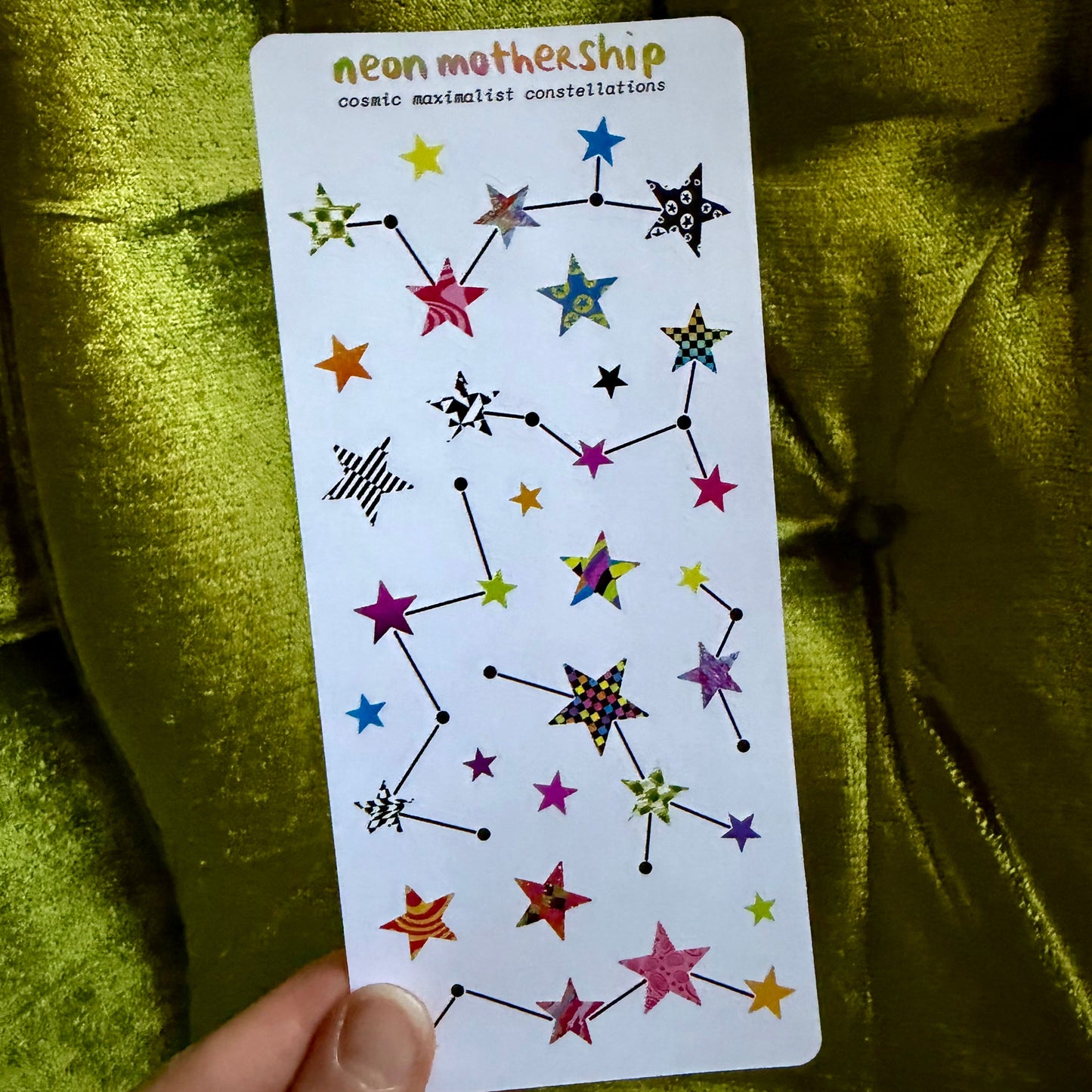 sticker sheet with colorful star and constellation designs held against a green fabric background