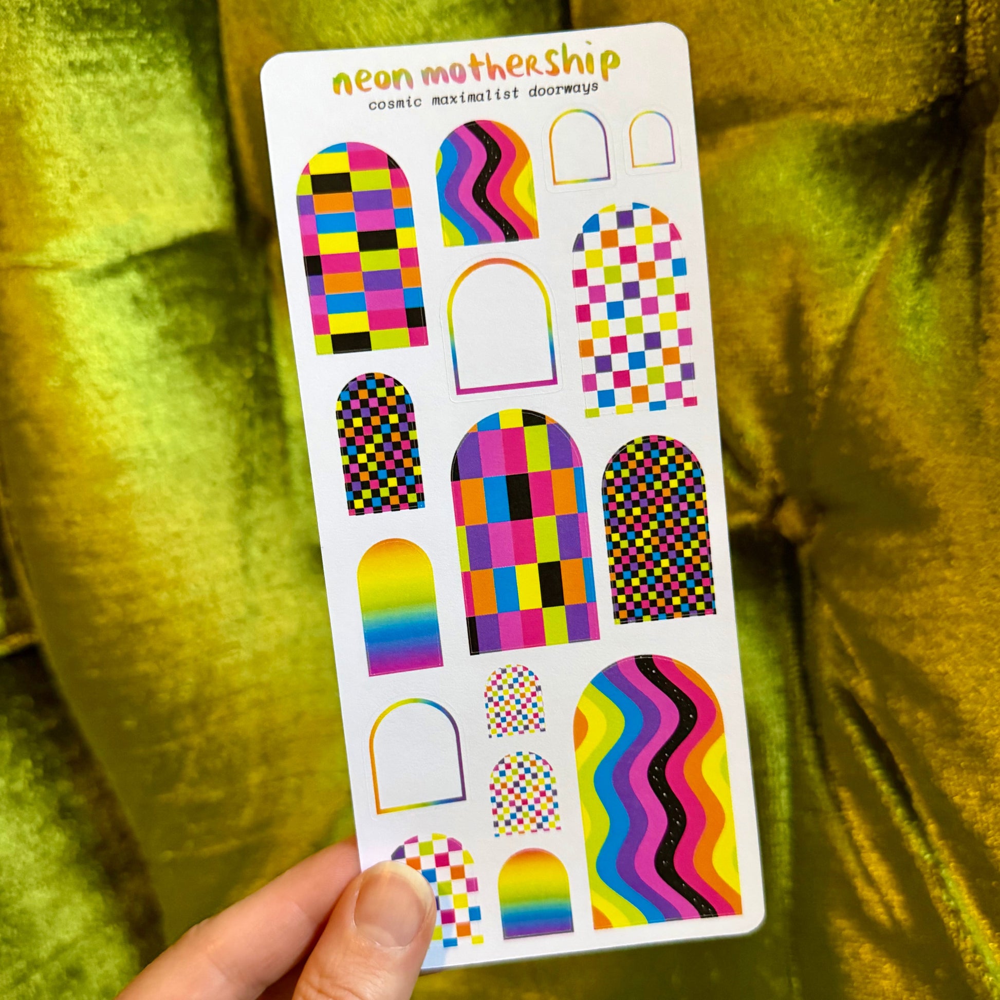 sheet of colorful arch shaped stickers held by a hand against a green background