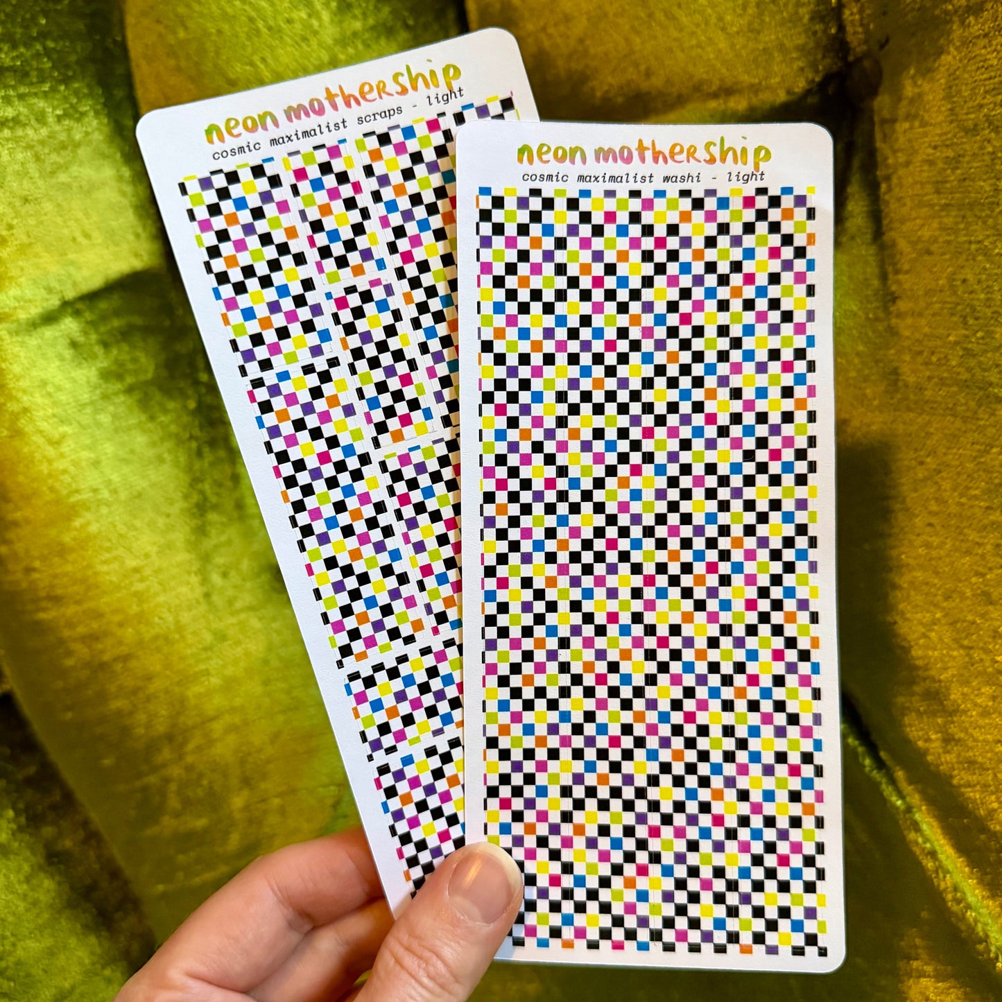 hand holding two checkered sticker sheets against a green background