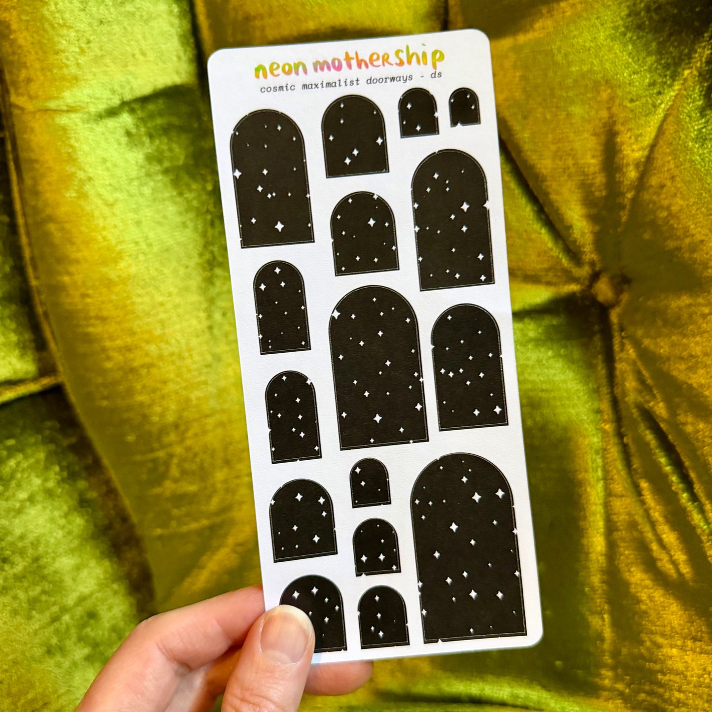sheet of arch shaped stickers held by a hand against a green background