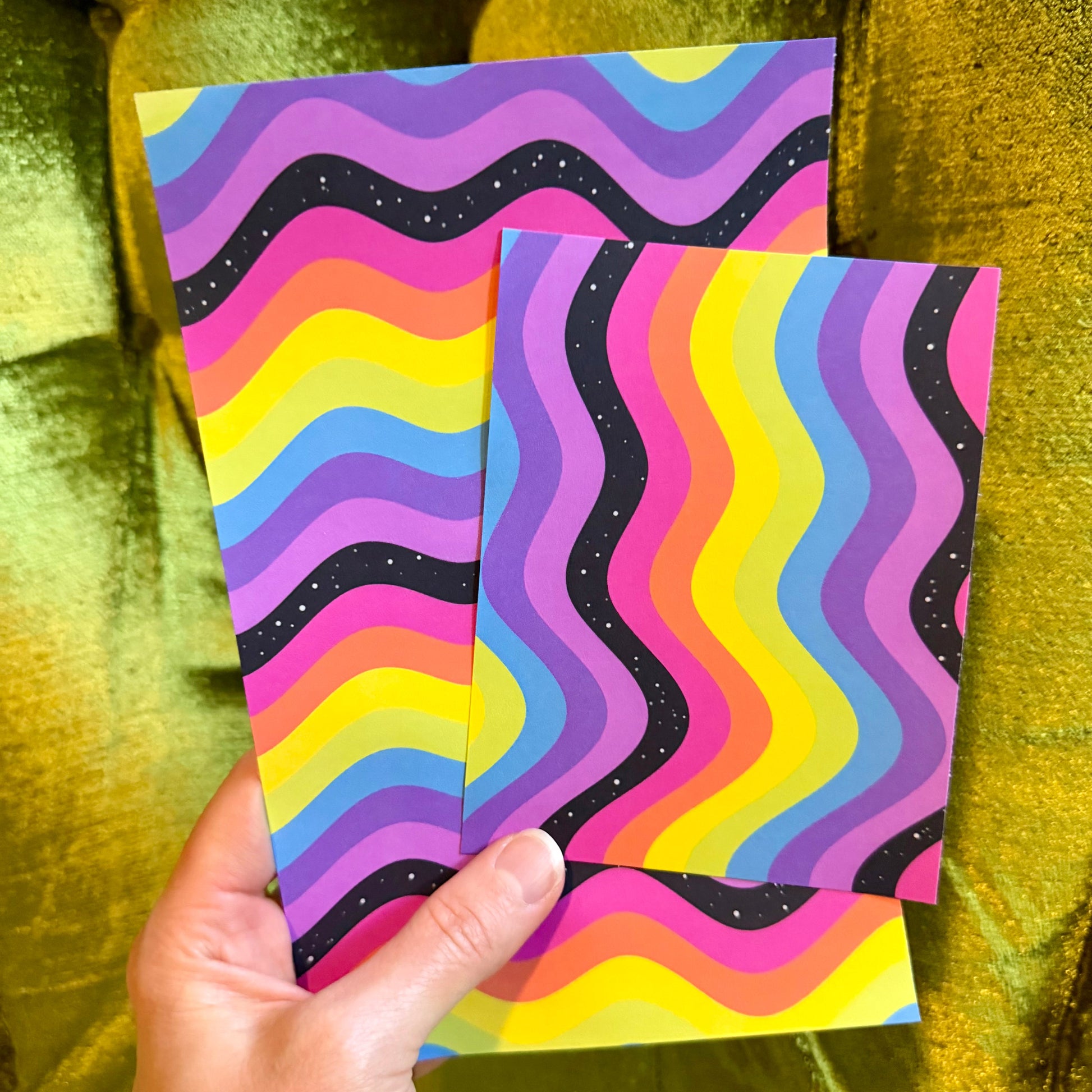 hand holding two rainbow sticker paper sheets against a green background