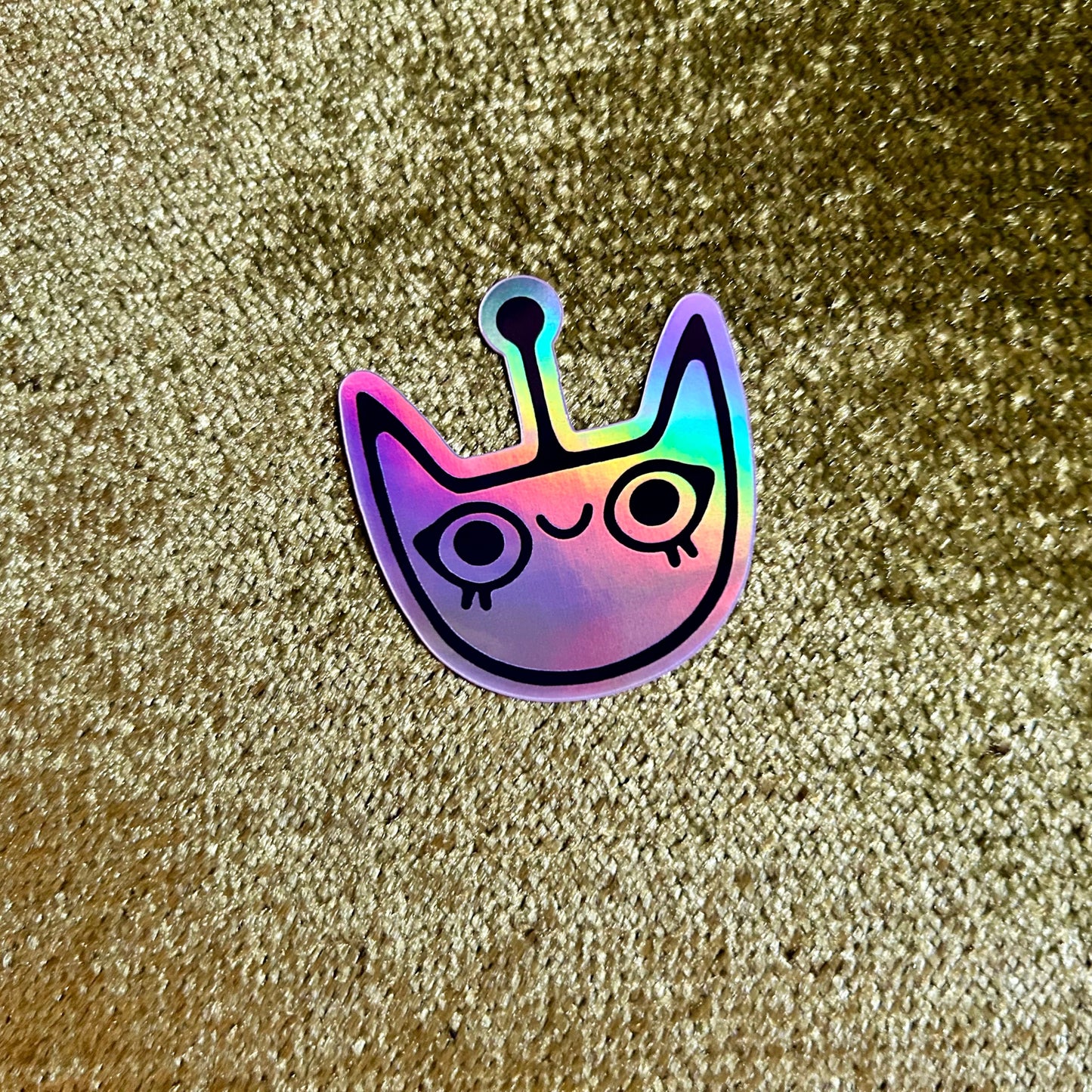 Holographic cat-shaped sticker on a glittery green background