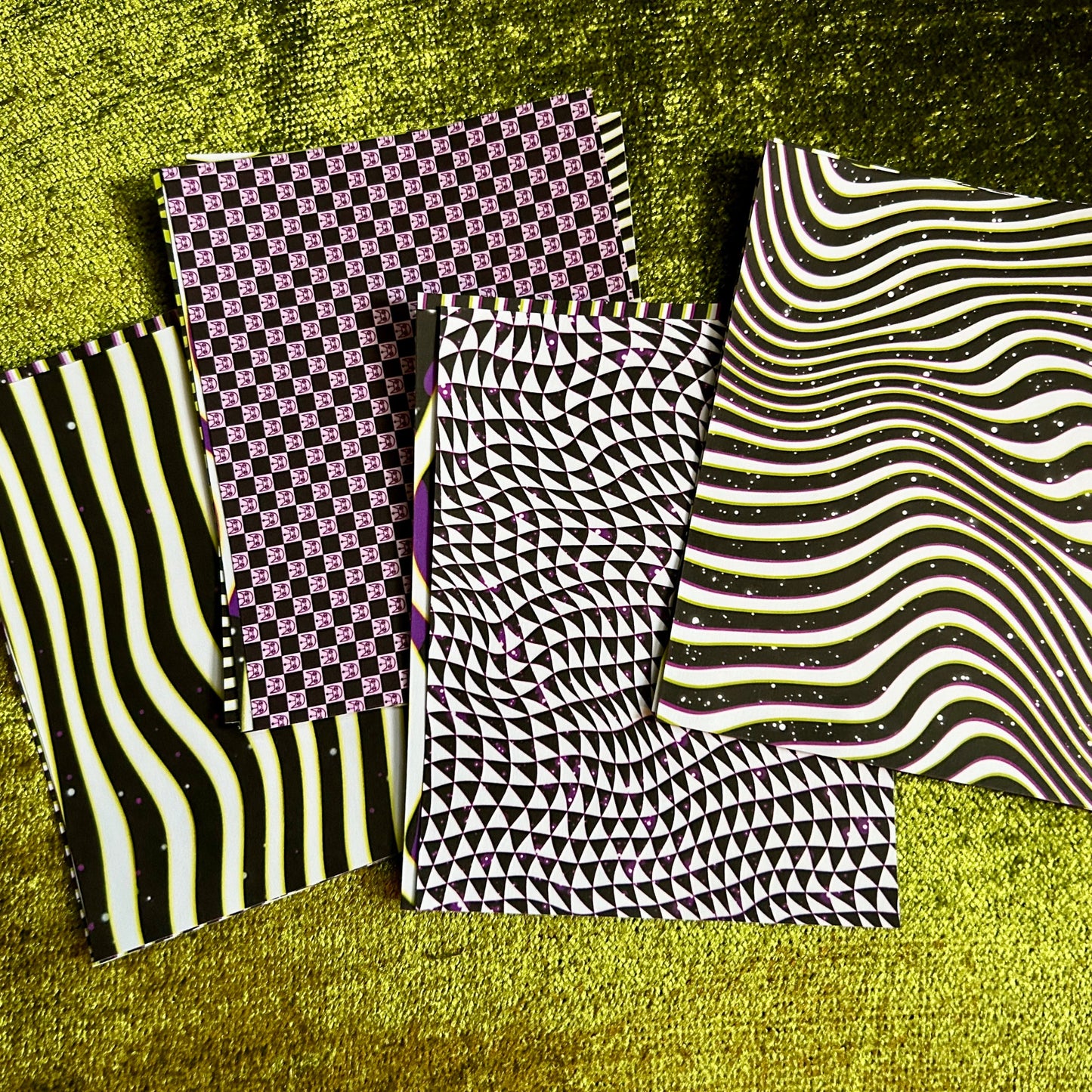 Four stacks of sticker sheets with different patterns on a textured green surface
