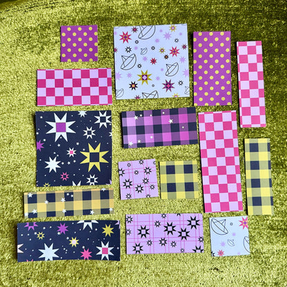 A collection of colorful patterned sticker scraps arranged on a textured olive green velvet surface. The pieces feature various patterns including pink checkers, yellow polka dots, black stars, purple plaid, and quilt star motifs.