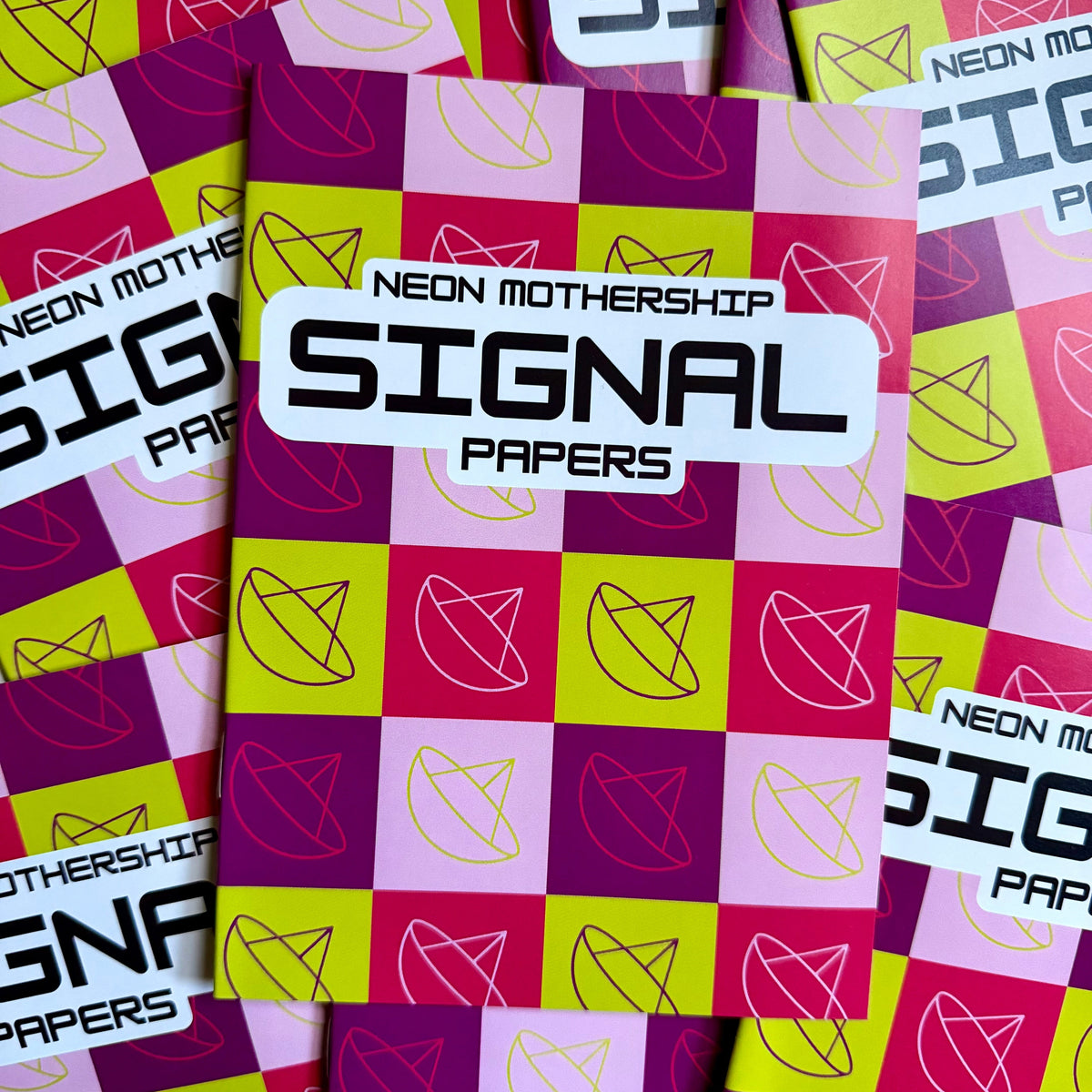 A stack of 'Signal Papers' by Neon Mothership, featuring a vibrant neon pink, purple, and lime green checkered pattern with minimalist line-drawn geometric shapes.
