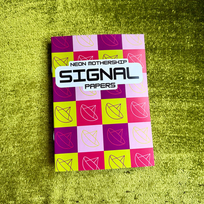 A notebook of neon checkered papers titled 'Signal Papers' by Neon Mothership, placed on a textured green surface.