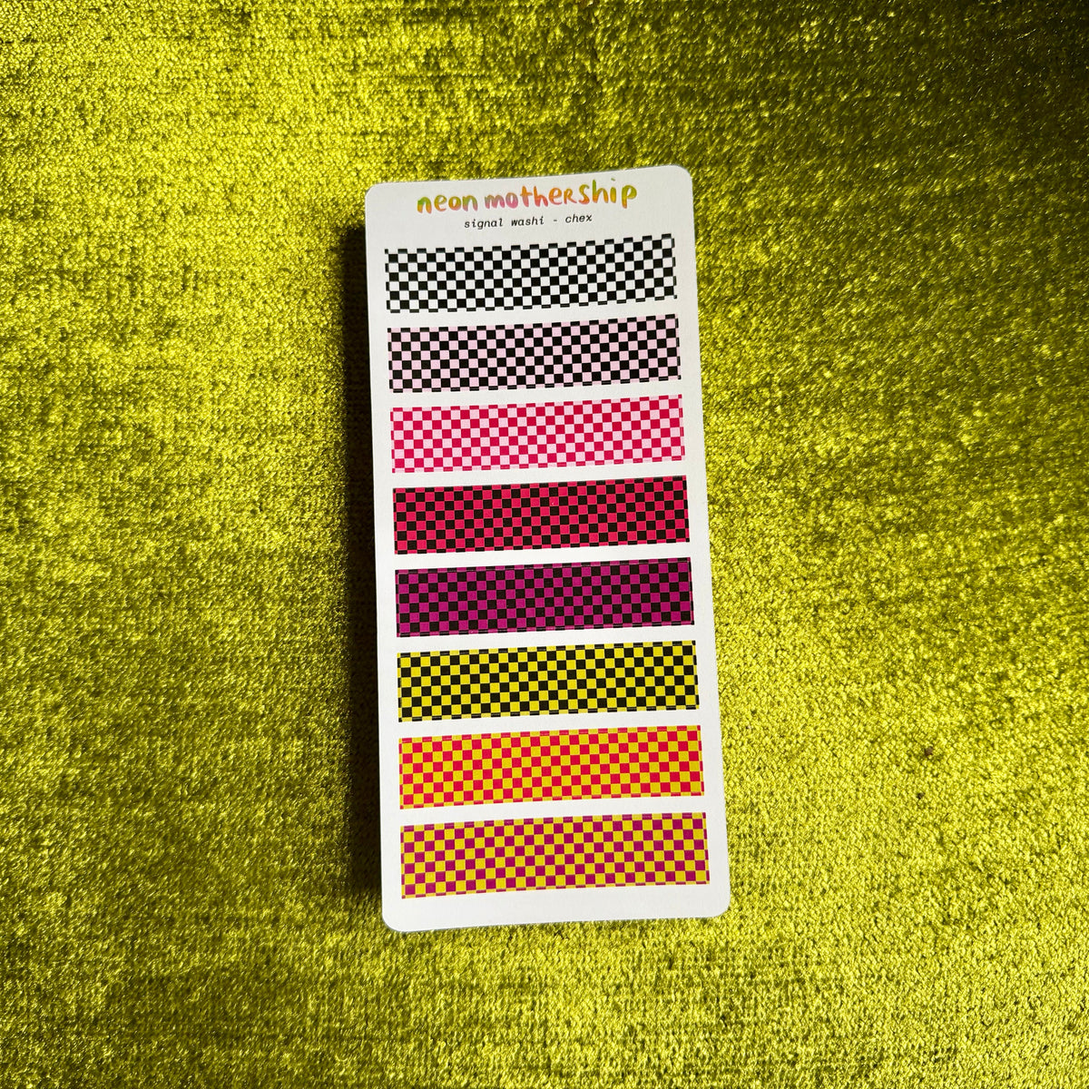 A card of washi tapes with various checkered patterns in black, pink, red, yellow, orange, and purple, displayed on a textured yellow background.