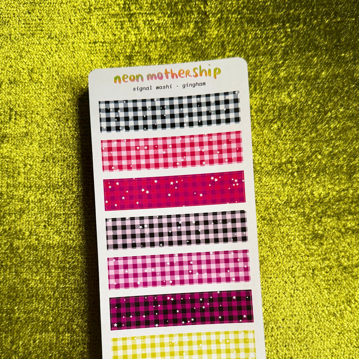 A sticker sheet featuring neon gingham and checkered washi tapes in pink, purple, yellow, and black, displayed on a textured yellow background.